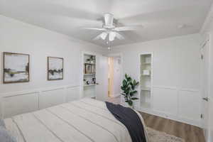 Bedroom featuring wood finished floors, ornamental molding, a decorative wall, a ceiling fan, and wainscoting