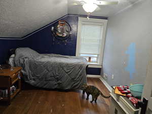 Bedroom featuring hardwood / wood-style floors, a textured ceiling, vaulted ceiling, multiple windows, and baseboards