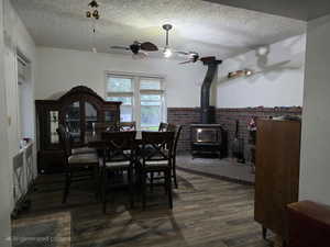 Dining space with ceiling fan, a wood stove, a textured ceiling, and wood finished floors