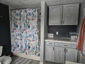Full bath featuring toilet, a textured ceiling, shower / bath combination with curtain, baseboards, and tile patterned floors
