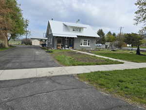 View of front facade with a front yard, an outdoor structure, a porch, metal roof, and stucco siding