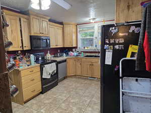 Kitchen featuring black appliances, a sink, a textured ceiling, light tile patterned flooring, and a ceiling fan