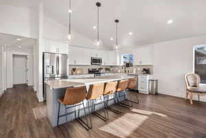 Kitchen with appliances with stainless steel finishes, dark wood-style flooring, a kitchen island, white cabinetry, and light countertops