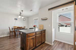 Kitchen with dark wood-style flooring, a peninsula, decorative light fixtures, and baseboards
