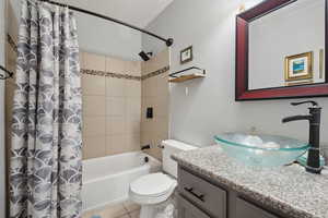 Full bath featuring vanity, shower / bath combo with shower curtain, toilet, and tile patterned flooring