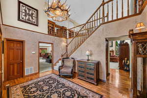 Foyer with hardwood / wood-style floors, a high ceiling, a chandelier, stairs, and baseboards