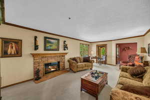 Carpeted living room featuring crown molding, a stone fireplace, baseboards, and a textured ceiling