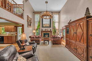 Living area with a chandelier, a high ceiling, healthy amount of natural light, a lit fireplace, and light carpet
