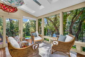 Sunroom / solarium with a skylight, vaulted ceiling, view of scattered trees, and a water view