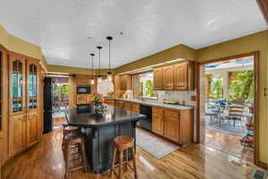 Kitchen featuring black appliances, a sink, a textured ceiling, a breakfast bar, and healthy amount of natural light