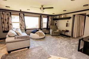 Carpeted living area featuring ornamental molding, a ceiling fan, and baseboards