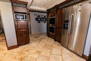 Kitchen featuring appliances with stainless steel finishes, stone tile floors, and dark brown cabinetry