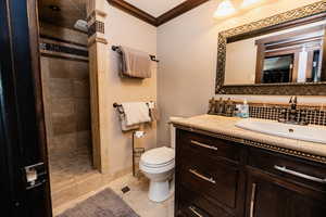 Bathroom featuring crown molding, tiled shower, toilet, vanity, and tile patterned floors