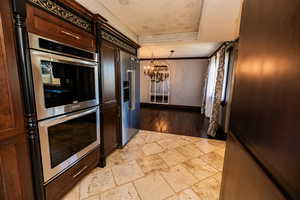Kitchen with a chandelier, a tray ceiling, stone tile floors, stainless steel double oven, and built in fridge