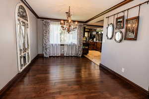 Dining room with crown molding, a chandelier, wood-type flooring, and baseboards