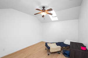 Living area with lofted ceiling, a ceiling fan, wood finished floors, a skylight, and a textured ceiling