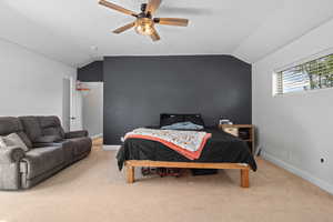 Carpeted bedroom with vaulted ceiling, baseboards, and ceiling fan