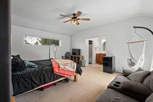 Bedroom featuring vaulted ceiling, light colored carpet, ensuite bathroom, ceiling fan, and a textured ceiling