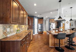 Kitchen with appliances with stainless steel finishes, a sink, dark wood finished floors, a kitchen bar, and decorative backsplash