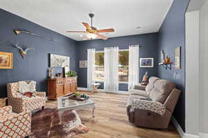 Living area with ceiling fan, light wood finished floors, a textured ceiling, and baseboards