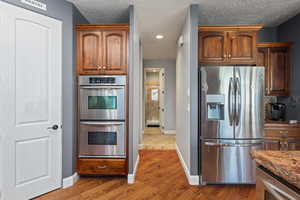 Kitchen with stainless steel appliances, wood finished floors, baseboards, stone counters, and a textured ceiling