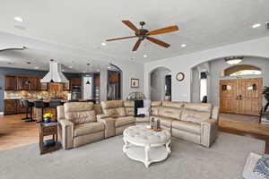 Living area with arched walkways, a ceiling fan, a textured ceiling, light wood-style floors, and recessed lighting