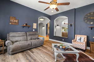 Living room with a ceiling fan, wood finished floors, arched walkways, baseboards, and a textured ceiling