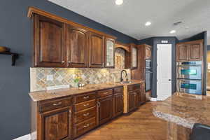 Kitchen featuring a sink, appliances with stainless steel finishes, hardwood / wood-style floors, light stone countertops, and decorative backsplash