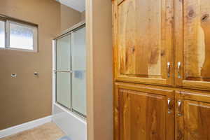Full bath with baseboards, combined bath / shower with glass door, and tile patterned flooring