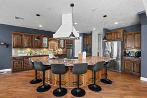 Kitchen with stainless steel appliances, decorative backsplash, light wood finished floors, light stone countertops, and a large island