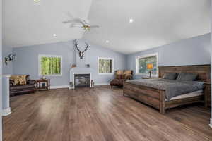 Bedroom featuring a glass covered fireplace, wood finished floors, lofted ceiling, baseboards, and recessed lighting