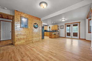 Living area featuring light wood-type flooring, wood walls, baseboards, and french doors