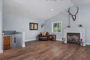 Living area with vaulted ceiling, wood finished floors, an upstairs landing, baseboards, and a glass covered fireplace