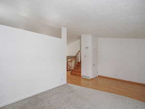 Empty room with stairs, light colored carpet, baseboards, a textured ceiling, and lofted ceiling