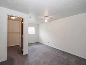 Unfurnished bedroom featuring dark colored carpet, a textured ceiling, ceiling fan, baseboards, and a spacious closet