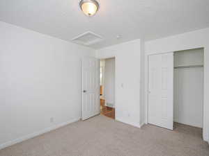 Unfurnished bedroom featuring attic access, carpet flooring, a textured ceiling, a closet, and baseboards