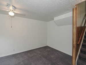 Additional living space with stairs, dark colored carpet, a ceiling fan, a textured ceiling, and baseboards