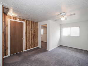Carpeted empty room featuring a ceiling fan, a textured ceiling, wood walls, and baseboards
