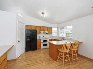 Kitchen with black fridge with ice dispenser, double oven range, under cabinet range hood, a sink, and light wood finished floors
