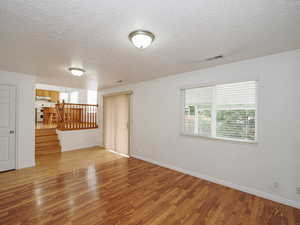 Empty room with wood finished floors, a textured ceiling, stairs, and baseboards