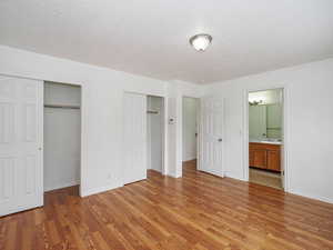 Unfurnished bedroom with two closets, light wood-style floors, a textured ceiling, and baseboards