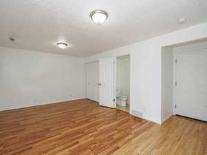 Empty room with light wood-type flooring, a textured ceiling, baseboards, and a smoke detector
