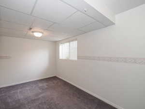 Spare room featuring dark colored carpet, a paneled ceiling, and baseboards
