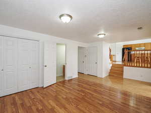 Unfurnished living room with wood finished floors, a textured ceiling, baseboards, and stairway