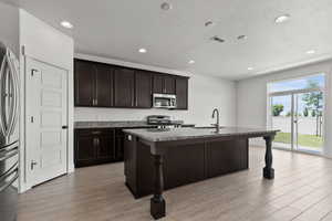 Kitchen with stainless steel appliances, light wood-style flooring, a sink, an island with sink, and recessed lighting