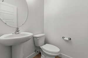 Half bath featuring baseboards, toilet, a sink, and wood finished floors