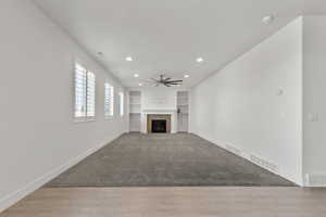 Unfurnished living room featuring a ceiling fan, baseboards, built in features, a fireplace, and recessed lighting