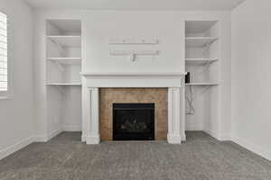 Unfurnished living room featuring a tiled fireplace, carpet flooring, and baseboards