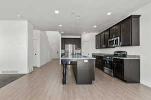 Kitchen with stainless steel appliances, recessed lighting, baseboards, light wood finished floors, and a kitchen breakfast bar