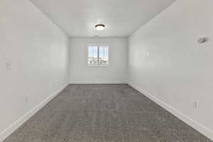 Unfurnished room featuring dark colored carpet and baseboards